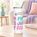 A white stainless steel skinny tumbler with a clear lid and metal straw, printed with "I'M FINE. IT'S JUST MY FACE." in pink, mint and lavender bubble letters under a rainbow shooting star.