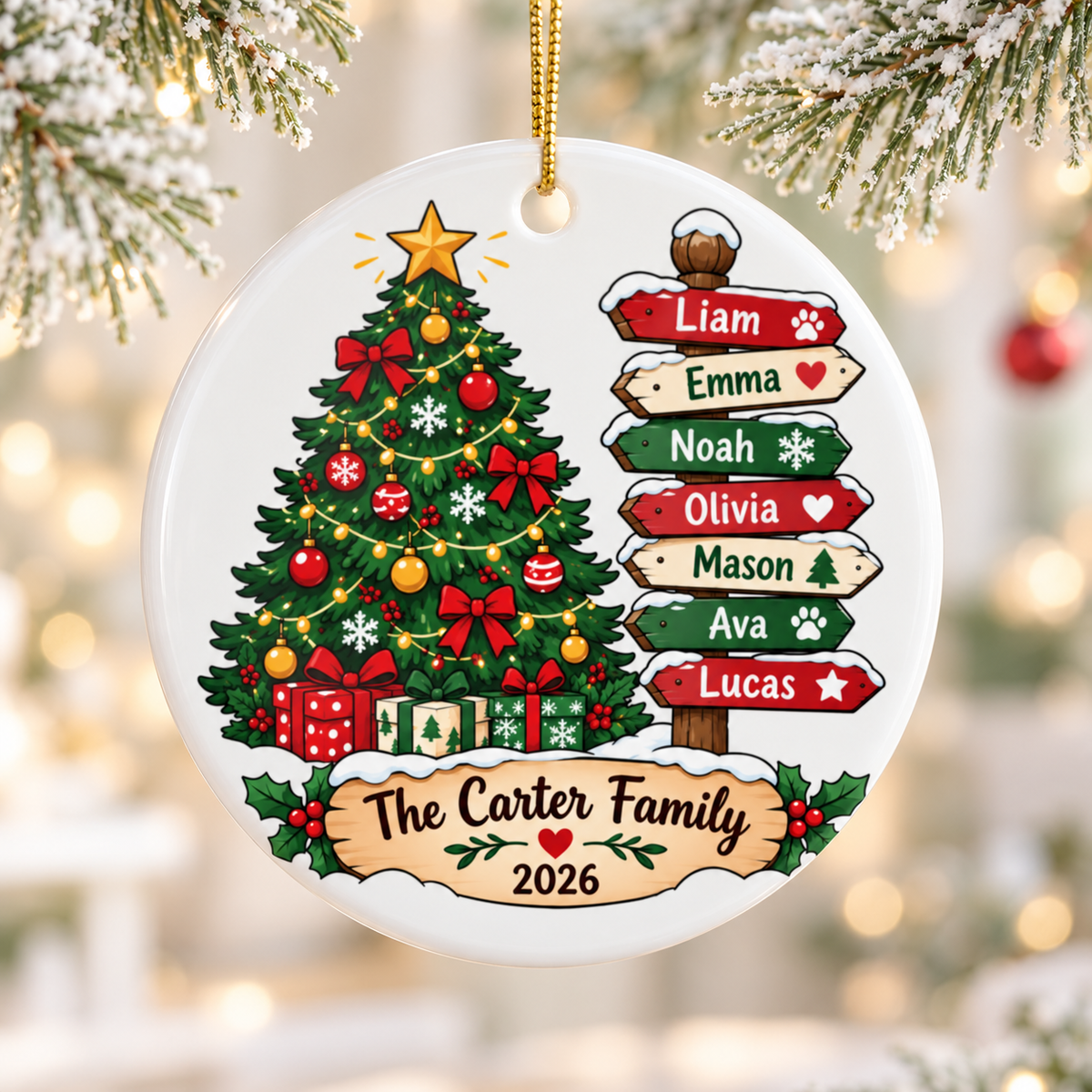 A round white ceramic Christmas ornament on a gold string, printed with a decorated Christmas tree with presents beside a snowy wooden signpost of red, cream and green arrows with sample family names, above a banner reading a sample family name and "2026".