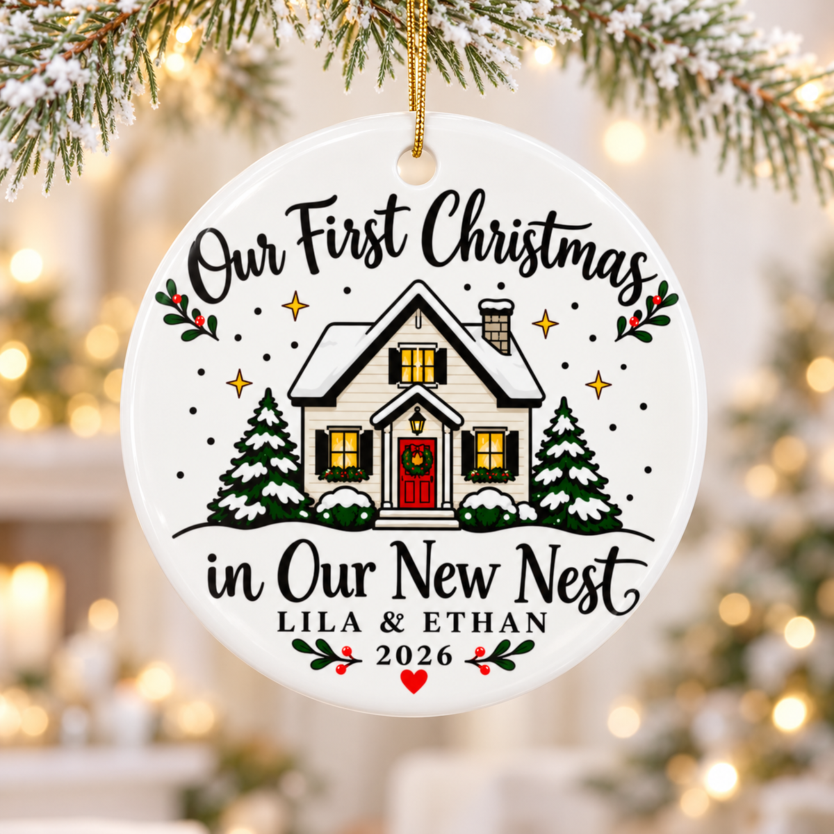A round white ceramic Christmas ornament on a gold string, printed with "Our First Christmas in Our New Nest" in black script around a snow-covered white house with a red door, glowing windows and snowy pine trees, with sample couple names, "2026" and a red heart.