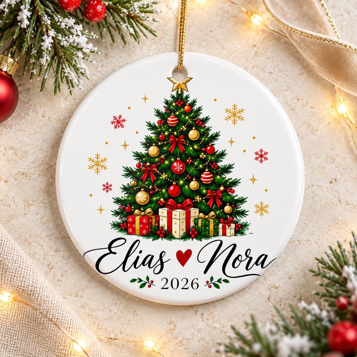 A round white ceramic Christmas ornament on a gold string, printed with a decorated Christmas tree with red and gold baubles, bows and wrapped presents under a gold star, above two sample names in black script joined by a red heart and "2026".