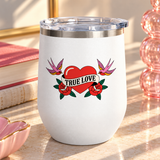 A white stainless steel stemless wine tumbler with a clear push-on lid, printed with a red heart wrapped in a "TRUE LOVE" banner between two red roses, with a pink swallow on each side, in retro tattoo style.
