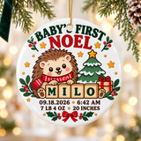 A round white ceramic Christmas ornament on a gold string, printed with "Baby's First Noel" in green and red lettering over a hedgehog in a red scarf holding wooden blocks spelling a sample name, beside a snowy tree and a present, above a sample birth date, time, weight and length.
