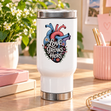 A white stainless steel travel mug with a silver lid and base, printed with "Love Grows Here" in white script on an anatomical heart in blue, red and purple, covered in daisies and small flowers.