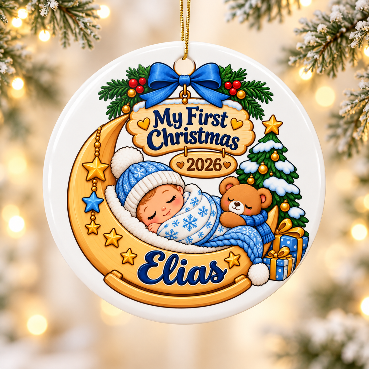 A round white ceramic Christmas ornament on a gold string, printed with a baby in a blue snowflake hat and blanket asleep on a golden crescent moon with a teddy bear, under a blue bow and a wooden "My First Christmas" and "2026" sign, beside a snowy tree, with a sample baby name in blue on the moon.