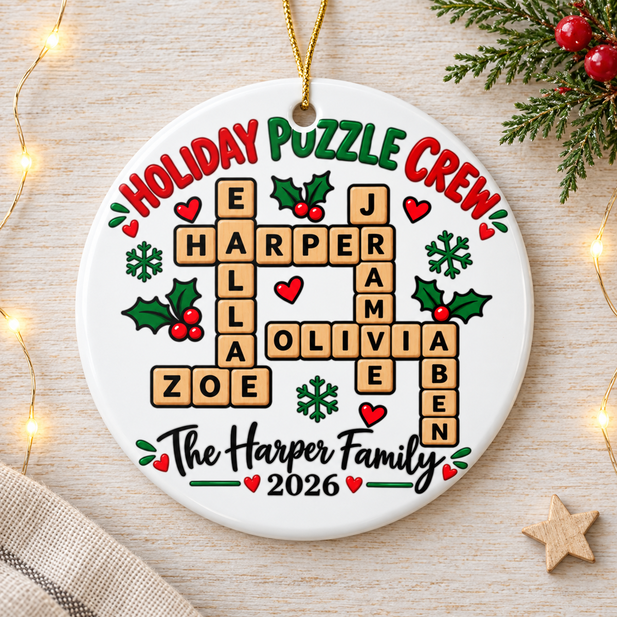 A round white ceramic Christmas ornament on a gold string, printed with "Holiday Puzzle Crew" in red and green lettering over sample first names linked in crossword-style letter tiles, with holly, hearts and snowflakes, above a sample family name in black script and "2026".
