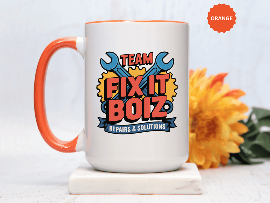 A white ceramic mug with a colored handle and interior, printed with "TEAM FIX IT BOIZ" in red lettering over crossed blue wrenches and yellow gears, above a blue "REPAIRS & SOLUTIONS" banner.