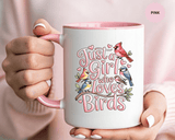 A white ceramic mug with a colored handle and interior, printed with "Just a Girl who Loves Birds" in pink lettering with a cardinal, blue birds and finches perched on a branch, with small hearts.