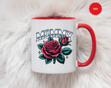 A white ceramic mug with a colored handle and interior, printed with "MOMMY" in silver-look block lettering above a large pink rose, a rosebud and teal leaves with small sparkles.