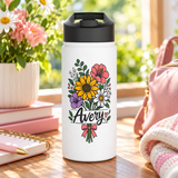 A white stainless steel water bottle with a black flip-top lid, printed with a wildflower bouquet with a yellow sunflower, a pink flower, a purple bloom and white daisies tied with a pink bow, the sample name "Avery" in black script across the stems and a small pink heart.