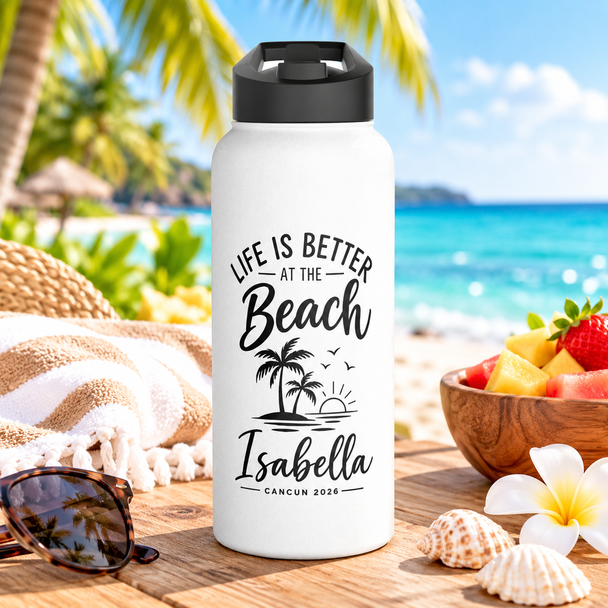 A white stainless steel water bottle with a black flip-top lid, printed with "Life Is Better at the Beach" in black lettering over two palm trees, a setting sun and birds, above the sample name "Isabella" in script and "Cancun 2026".