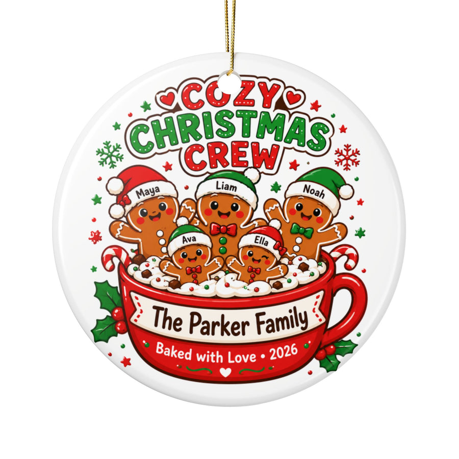 A round white ceramic Christmas ornament on a gold string, printed with "COZY CHRISTMAS CREW" above five gingerbread people in Santa hats, each with a sample name, in a red mug reading "The Parker Family, Baked with Love 2026".