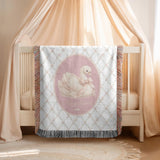 White fringed woven blanket on a cream crib, printed with a floral trellis and a central pink oval holding a white swan in a pale bow, with the name Mary Grace in cream script.