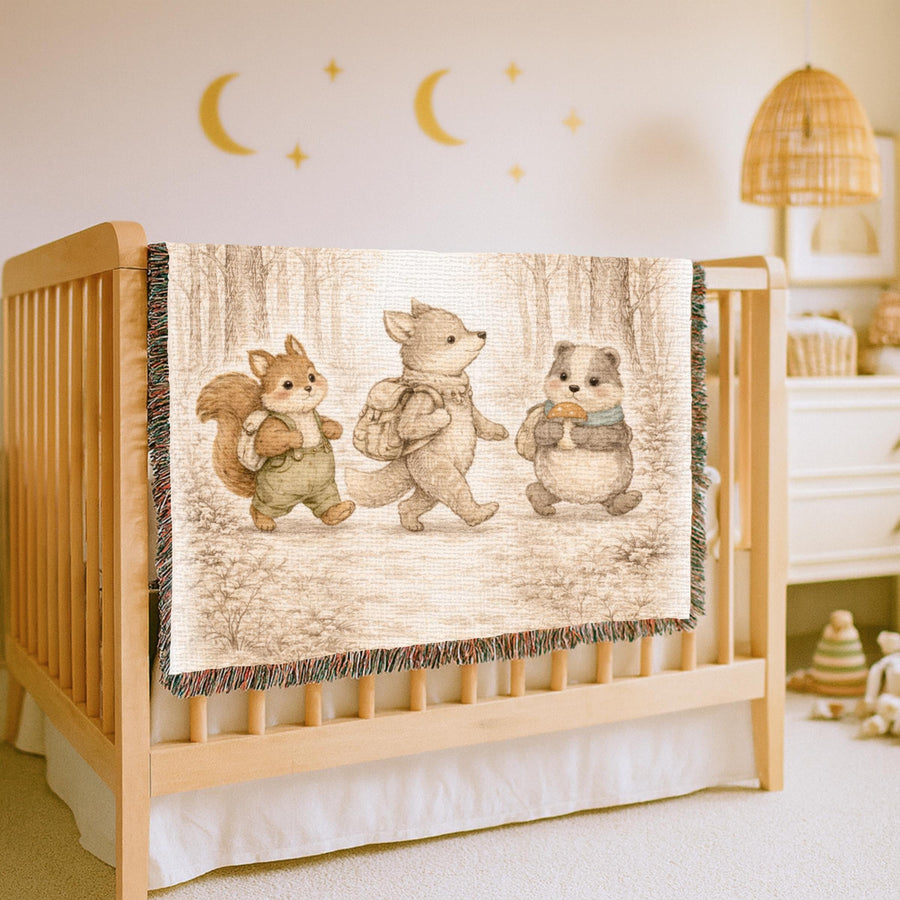 Cream fringed woven blanket printed in soft sepia with a squirrel, a wolf cub and a badger walking in single file through bare winter woodland, each carrying a small backpack.