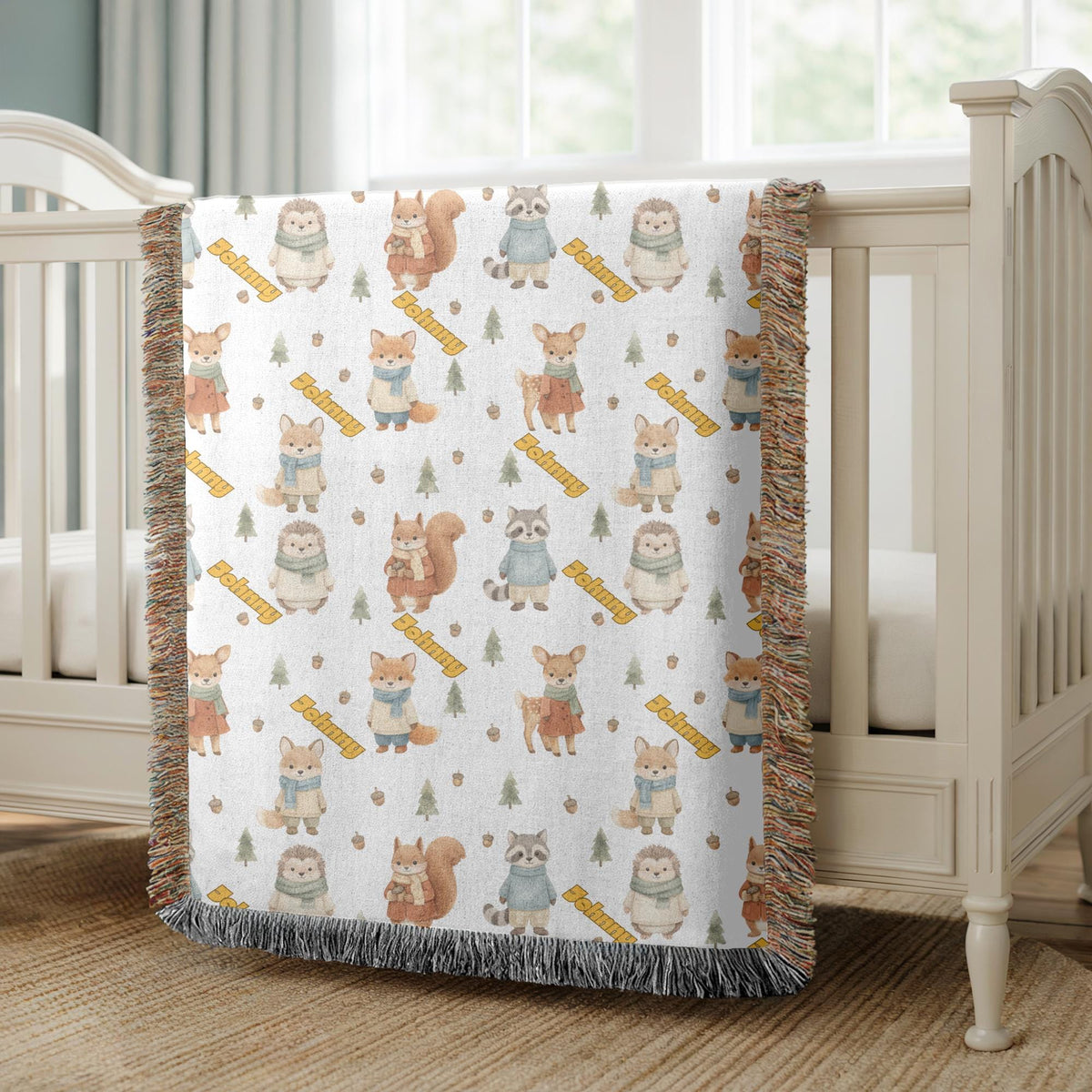 White fringed woven blanket printed with watercolour woodland animals in scarves, hedgehogs, squirrels, foxes and a deer, among acorns, small trees and yellow banners reading Johnny.
