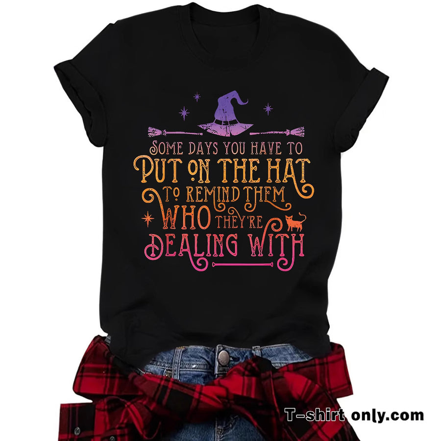 A black T-shirt printed with a purple witch hat and broomstick above Some days you have to put on the hat to remind them who they're dealing with in gradient lettering.