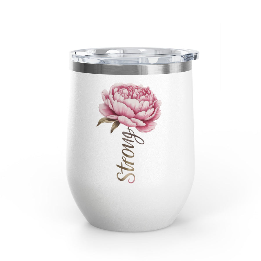 A white stainless steel wine tumbler with a clear push-on lid, printed with a large pink peony flower and the word "Strong" in brown script beneath it, on a table near a lake.