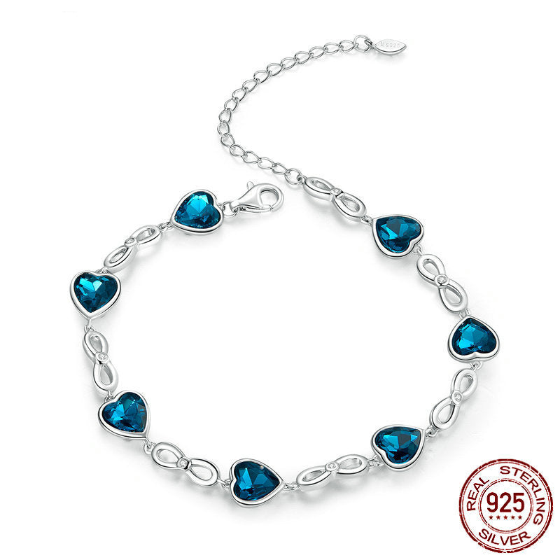 Silver bracelet with blue heart-shaped crystal charms and infinity link design, on white background