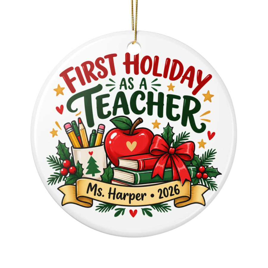 A round white ceramic Christmas ornament on a gold string, printed with "FIRST HOLIDAY AS A TEACHER" in red and green lettering above a red apple, a cup of pencils, stacked books with a red bow and holly, and a banner with a sample teacher name and "2026".