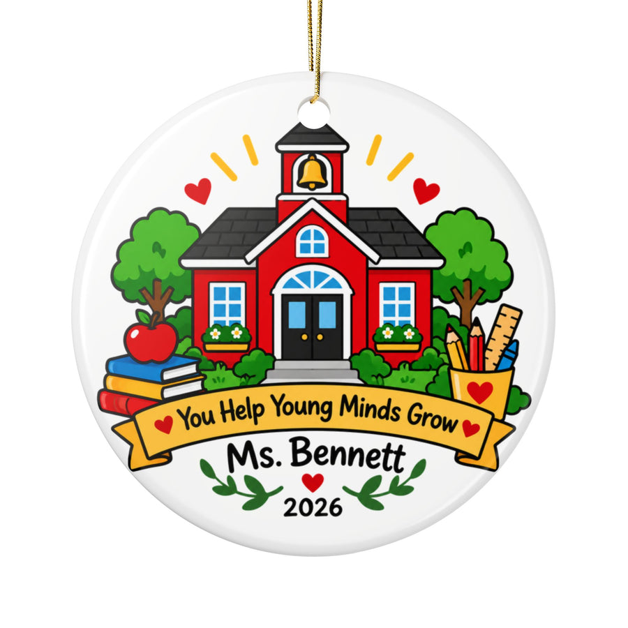 A round white ceramic Christmas ornament on a gold string, printed with a red schoolhouse with a bell tower between green trees, an apple, stacked books and a cup of pencils and a ruler, above a yellow banner reading "You Help Young Minds Grow", a sample teacher name and "2026".