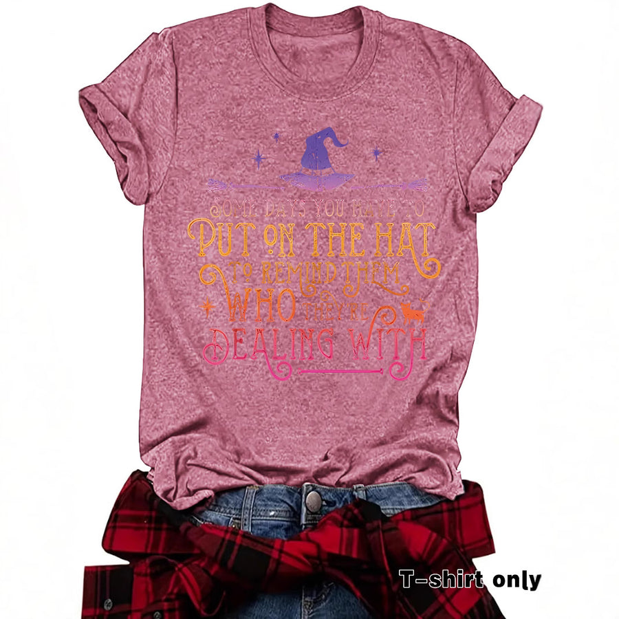 A black T-shirt printed with a purple witch hat and broomstick above Some days you have to put on the hat to remind them who they're dealing with in gradient lettering.
