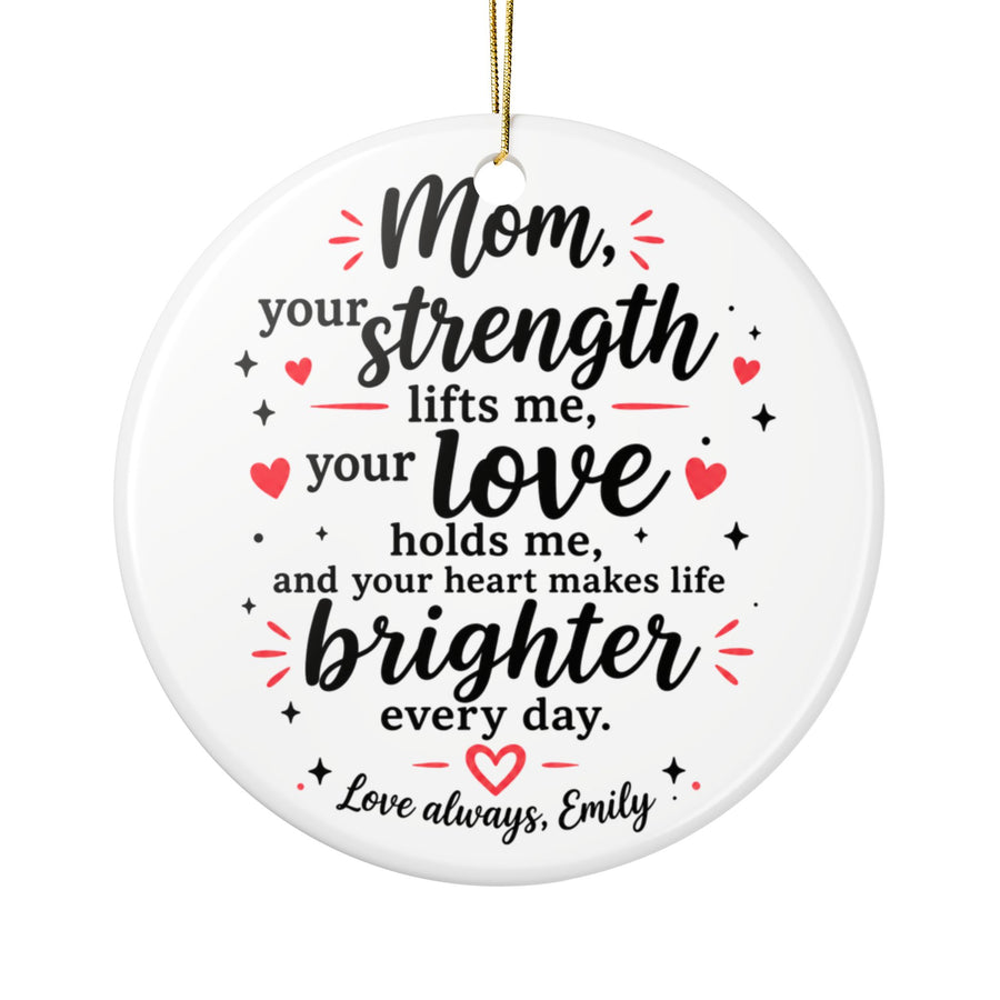 A round white ceramic Christmas ornament on a gold string, printed with a verse in black script, "Mom, your strength lifts me, your love holds me", with red hearts and a sample "Love always" signature.