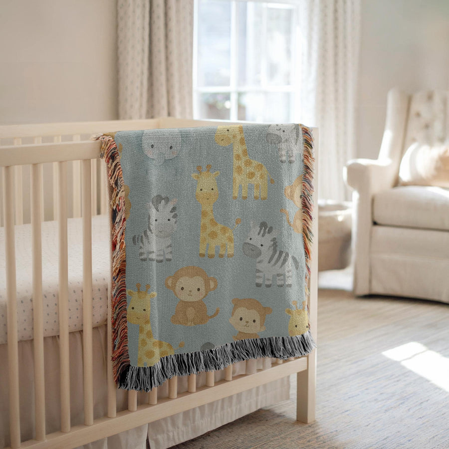 Fringed woven blanket in pale sage, printed with watercolour safari animals, giraffes, zebras, an elephant, a lion and monkeys, spaced evenly between small green leaves and sprigs.