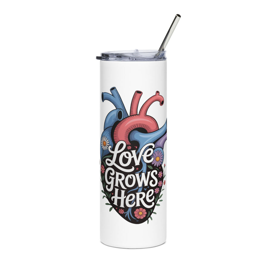 A white stainless steel skinny tumbler with a clear lid and metal straw, printed with "Love Grows Here" in white script on an anatomical heart in blue, red and purple, covered in daisies and small flowers.