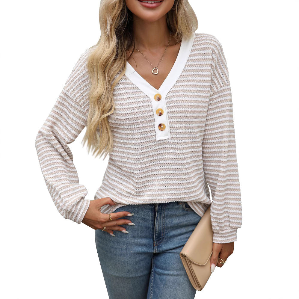 A woman wearing a long sleeved waffle knit top finely striped in oatmeal and white, with a white V neck placket and three wooden buttons at the chest, over blue jeans, one hand tucked into a back pocket.