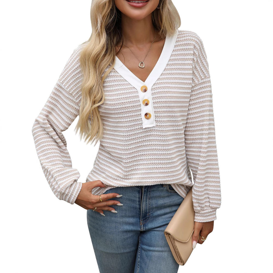 A woman wearing a long sleeved waffle knit top finely striped in oatmeal and white, with a white V neck placket and three wooden buttons at the chest, over blue jeans, one hand tucked into a back pocket.