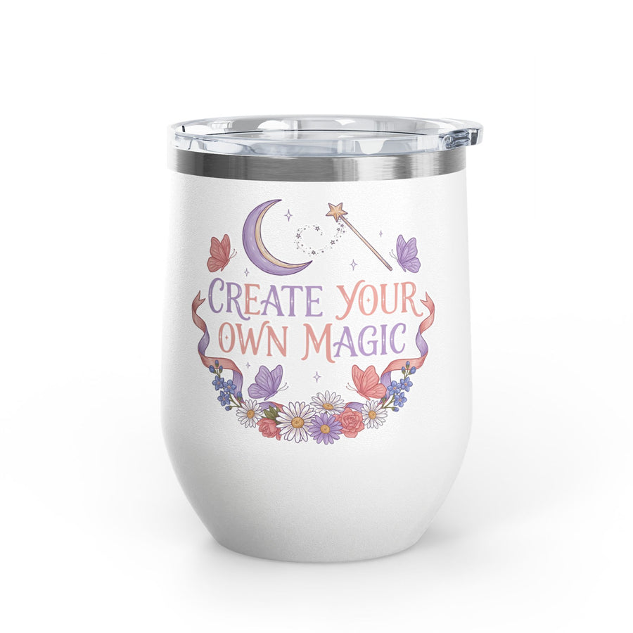 A white stainless steel stemless wine tumbler with a clear push-on lid, printed with "CREATE YOUR OWN MAGIC" in lilac and coral lettering under a crescent moon and a star wand, framed by butterflies, ribbons and flowers.