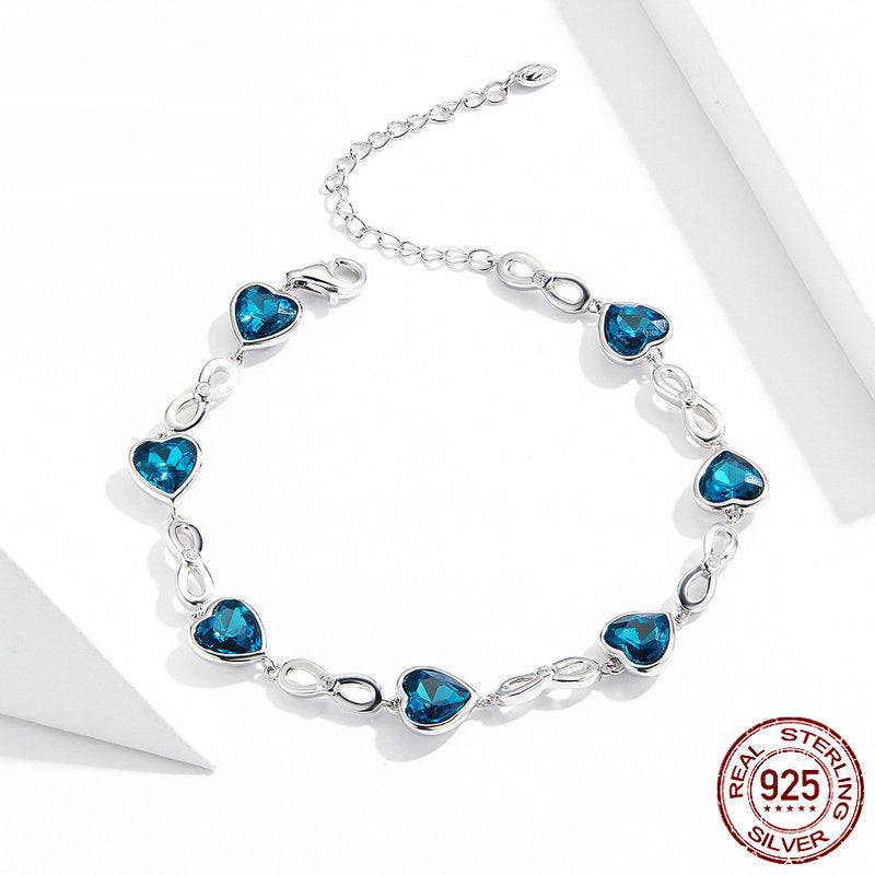 Silver bracelet with blue heart-shaped crystal charms and infinity link design, on white background