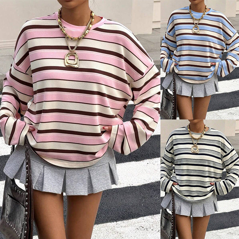 A woman wearing an oversized sweatshirt striped in pink, cream and deep brown with dropped shoulders and long full sleeves, worn over a grey pleated mini skirt, a studded dark bag on one arm.