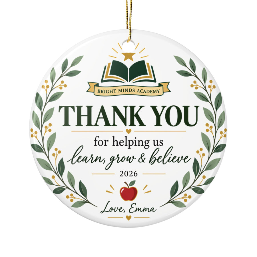 A round white ceramic Christmas ornament on a gold string, printed with an open green book under a gold star on a banner with a sample school name, "THANK YOU for helping us learn, grow & believe", "2026", an apple and a "Love" signature, framed by a leafy wreath.