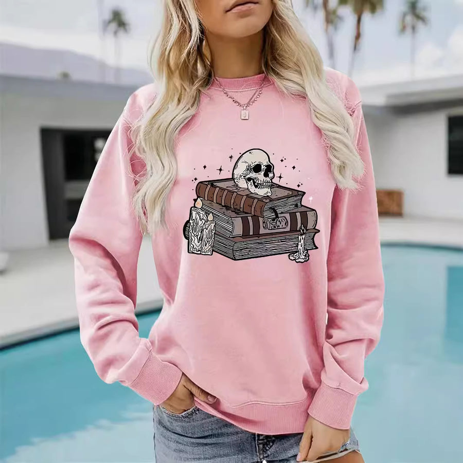 A pink crewneck sweatshirt printed with a skull resting on a stack of old spell books and potion bottles.