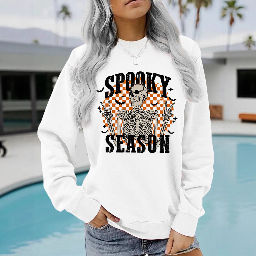 A red crewneck sweatshirt printed with a skeleton making peace signs in front of an orange checkerboard under the words Spooky Season.