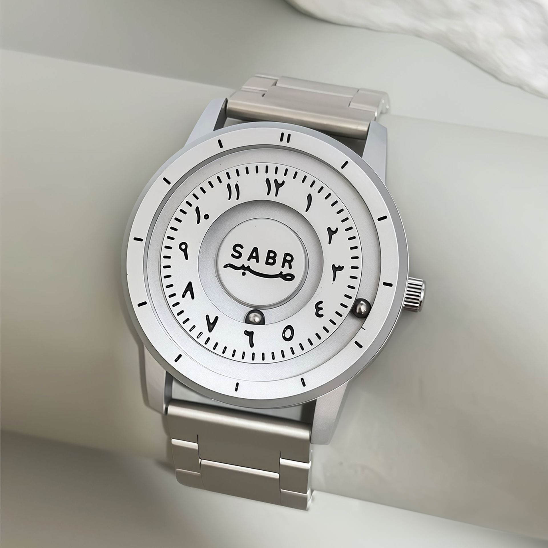 White dial quartz watch with Arabic numerals, the word SABR, and a silver stainless steel bracelet