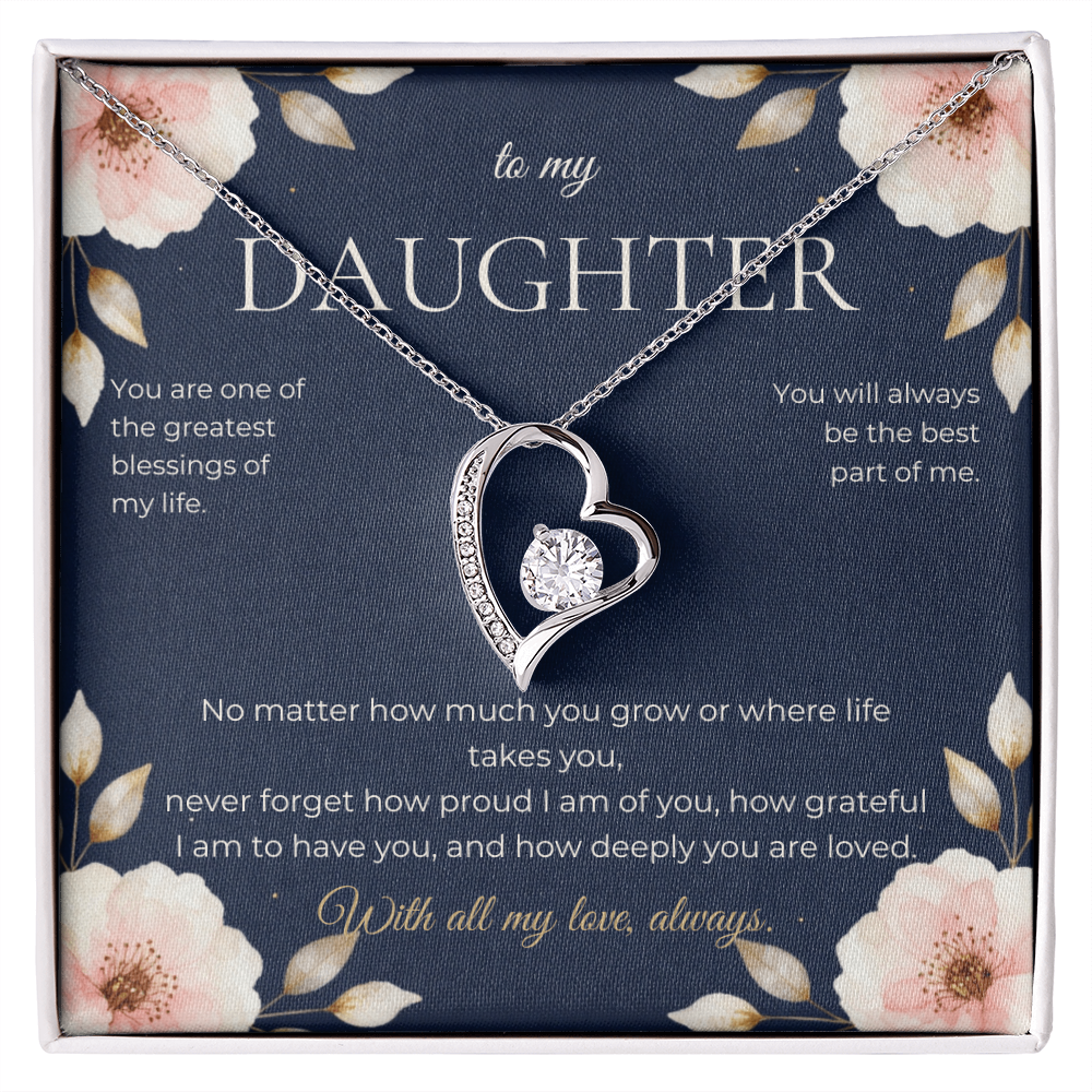 Silver heart-shaped pendant set with a solitaire stone and a row of small stones, displayed in a gift box on a navy card headed to my Daughter and framed with pink blossoms.