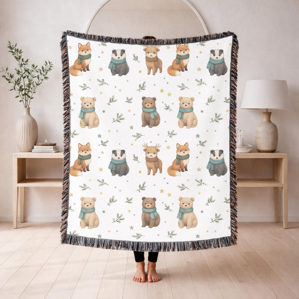 White fringed woven blanket printed with watercolour foxes, badgers, bears and a deer in pale teal scarves, set in rows among small gold stars and sprigs of green foliage.
