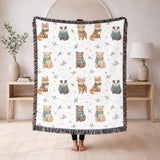 White fringed woven blanket printed with watercolour foxes, badgers, bears and a deer in pale teal scarves, set in rows among small gold stars and sprigs of green foliage.