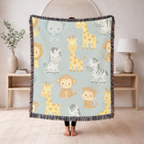 Fringed woven blanket in pale sage, printed with watercolour safari animals, giraffes, zebras, an elephant, a lion and monkeys, spaced evenly between small green leaves and sprigs.