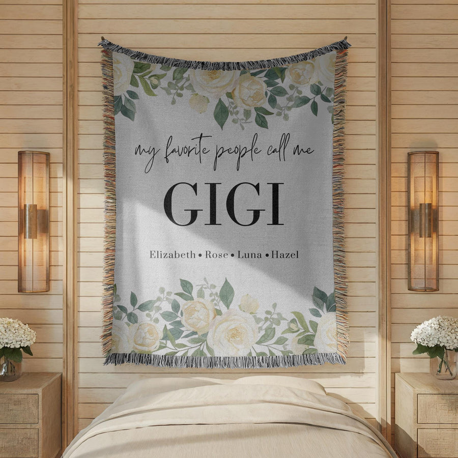Grey fringed woven blanket printed with white roses and eucalyptus along the top and bottom, reading my favorite people call me Gigi above the names Elizabeth, Rose, Luna and Hazel.